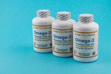 24.03.25 Lviv Ukrayna. Mavi arka planda üç şişe Omega-3 prim balık yağı bulunur. Her şişede, sağlık için önemli yağ asitleri içeren besin takviyeleri bulunur..