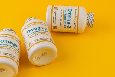 24.03.25 Lviv Ukrayna Üç şişe Omega-3 prim balık yağı parlak sarı bir yüzeye yerleştirilir. Her şişede ürün ve besin bilgileri yer alıyor.