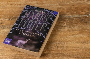 25.03.25 Lviv Ukrayna. Harry Potter kitaplarının bir koleksiyonu ahşap bir masanın üzerinde duruyor. Üçüncü kitabın Fransızca baskısı bir geyiğin büyüleyici sanat eserini gösteriyor, entrika ekliyor.