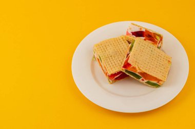 Canlı reçelli waffle kekleri beyaz bir tabakta mükemmel bir şekilde hazırlanmış krema, yoğurt, sulu kivi, çilek ve ahududu katmanları sergilenmeye hazır..