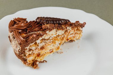 Bir dilim zengin çikolata katmanlı kek beyaz bir tabakta oturup lezzetli tabaklarını ve tatlı aşıkları için mükemmel bir bisküvi garnitürü sergiliyor..