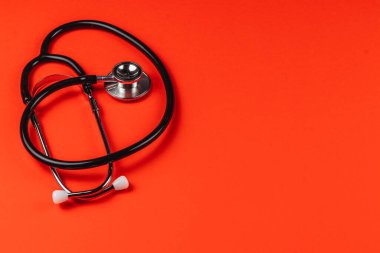 Stetoskop çarpıcı bir kırmızı arkaplana karşı düz bir şekilde uzanır ve sağlık hizmetlerindeki önemini vurgular. Bu tıbbi araç profesyonellerin ithafını temsil ediyor..