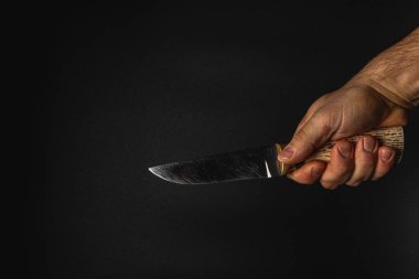 Bir insan bıçağı sıkıca kavrar ve bıçağını düşük ışıkta gösterir. Odaklanma, bıçağın detaylarını karanlık bir arkaplanda vurguluyor..