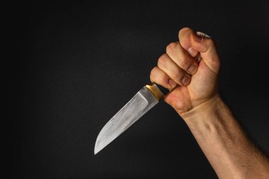 Güçlü bir el keskin bir bıçağı sıkıca tutar, parıltısını siyah bir zemine karşı gösterir. Bıçak ve kavramanın detaylarına odaklanarak, hazır olmanın önemini vurgulamak..