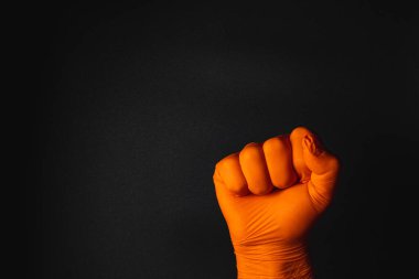 Eldivenli bir yumruk karanlık bir arkaplana dayanır, gücü ve meydan okumayı simgeler. Turuncu eldiven sahneye çarpıcı bir kontrast ekler..
