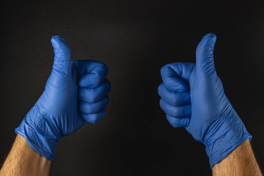 Mavi eldiven giyen iki el baş parmaklarıyla kaldırılır. Bu da basit, karanlık bir ortamda tatmin ya da onay anlamına gelir..