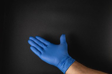 Mavi eldivenle kaplı bir el koyu bir arka plana uzanıyor. Karşıtlık eldiveni vurgular ve görsel sunuma derinlik ekler.