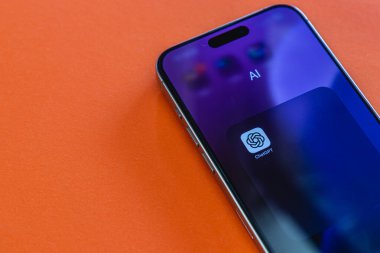 03.26.25 Lviv Ukrayna Parlak turuncu bir yüzeye sahip parlak bir akıllı telefon, ekranında yapay zeka uygulamasını gösteriyor, teknolojinin ve yeniliğin özünü yakalıyor..