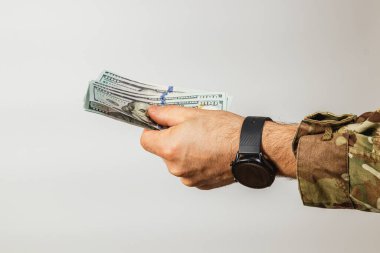 Bir el birkaç banknot uzatıyor, askeri tarzda bir üniforma sergiliyor. Bu jest, tarafsız bir ortamda gerçekleşen finansal bir alışveriş ya da yardımı işaret ediyor..