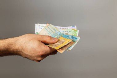 Bir el uzanıyor, farklı banknotlardan oluşan banknotların karışımını gösteriyor, para biriminin çeşitliliğini gösteriyor. Arka plan sade, paranın altını çiziyorum..