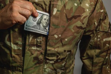 Kamuflaj üniformalı bir asker cebine 100 dolarlık banknot koyuyor ve bir anlık para değişimi ya da alım satımı yapıyor..