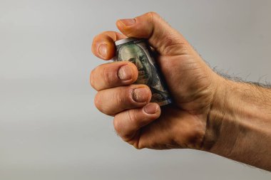 Bir insan elindeki 100 dolarlık banknotu sıkıca kavrayıp güç gösterisi sergiliyor. Arkaplan tarafsız ve sade..