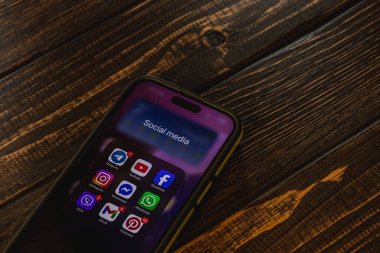 03.26.25 Lviv Ukrayna. Ekranda çeşitli sosyal medya simgelerine sahip bir akıllı telefon desenli ahşap bir masada oturuyor. Ayarlar sıcak ve davetkar bir atmosfer sağlıyor, gündelik tarama için ideal..