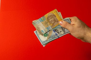 Bir el çeşitli banknotlar tutar, hem yerel hem de yabancı para birimlerini canlı kırmızı bir zemine karşı sergiler, para değişimi kavramını gözler önüne serer.