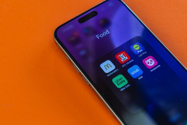 03.26.25 Lviv Ukrayna. Bir akıllı telefon parlak turuncu bir yüzeye dayanır ve çeşitli gıda dağıtım uygulamaları sergiler. Ekran uygun yemek seçenekleri için seçenekleri vurgular.