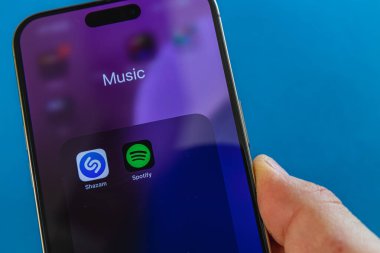 03.26.25 Lviv Ukrayna. Bir el müzik uygulamalarını gösteren bir akıllı telefon tutuyor. Ekranda Shazam ve Spotify simgeleri yer alıyor. Parlak renkler modern teknoloji ortamını vurgular.