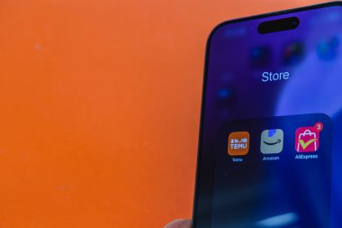 03.26.25 Lviv Ukrayna Bir el akıllı telefonu parlak turuncu bir duvara dayayıp çeşitli alışveriş uygulamalarını gösteriyor. Renkli simgeler sahneye neşeli bir dokunuş ekler.