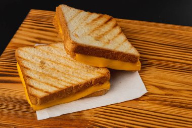 İki mükemmel ızgara peynirli sandviç ahşap bir tahtanın üzerinde oturur, üzerinde kahverengi tost ve erimiş peynir sergilenir. Kahvaltı, brunch, öğle yemeği ya da lezzetli bir atıştırmalık için idealdir..
