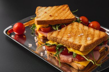 Bu lezzetli ızgara peynirli sandviç, jambon, ıspanak, roka ve iki mükemmel kızarmış ekmek arasında katmanlanmış taze domatesler içerir. Öğle yemeği veya brunch için ideal..