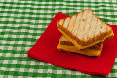 Eritilmiş peynir, kırmızı peçeteye istiflenmiş iki dilim mükemmel ızgara sandviçten dökülür. Konforlu bir brunch 'ın ya da canlı bir masa örtüsünün üzerinde atıştırma vaktinin tadını çıkarıyordu..