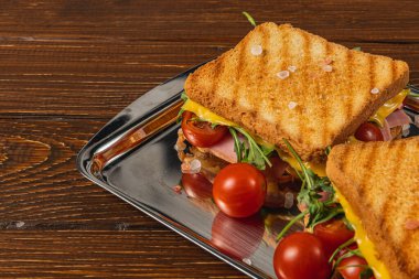 Jambon, ıspanak, roka ve olgun domateslerle dolu leziz bir ızgara peynirli sandviç, parlak gümüş bir tepside oturur, hızlı bir öğle yemeği ya da atıştırmalık için mükemmeldir, sizi kazmaya davet eder..