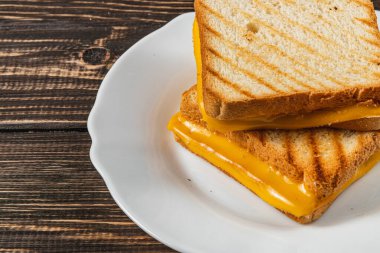 Kusursuz bir ızgara peynirli sandviç beyaz bir tabakta servis edilir, erimiş peyniri iki dilim altın rengi tost ekmeğinin arasında sergiler. Öğle yemeği, brunch ya da lezzetli bir atıştırmalık için ideal..