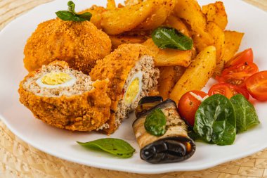 Canlı bir tabakta, kıtır patates dilimleri ve taze vişneli domateslerin yanı sıra lezzetli tatlar içeren, altın-kahverengi doldurulmuş et sergileniyor..