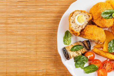 Bir tabakta kroket ve doldurulmuş sebzeler de dahil olmak üzere çeşitli çıtır çerezler yer. Taze domates ve ıspanak bambu hasırı üzerinde sunulan canlı bir renk ekler..