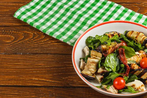 Izgara sebze, canlı ıspanak ve vişneli domatesli taze hazırlanmış salata. Tahta bir masaya karşı beyaz bir kasede damalı kumaşla servis edilmiş..