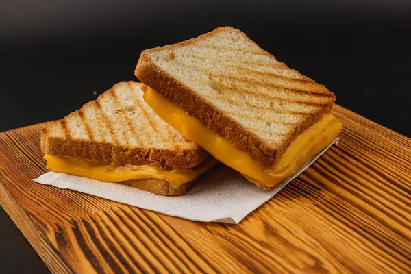 Tahta bir tahtanın üzerine yerleştirilmiş kızarmış ekmeğin arasında erimiş altın peynirli leziz peynirli sandviç. Kahvaltı, brunch ya da lezzetli bir öğle yemeği için ideal bir seçim..