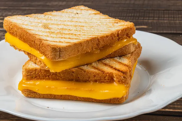 İki mükemmel ızgara peynirli sandviç, beyaz bir tabakta istiflenmiş, içinde altın tost ekmeği ve erimiş peynir var. Kahvaltı, brunch ya da aperatif için her zaman ideal..