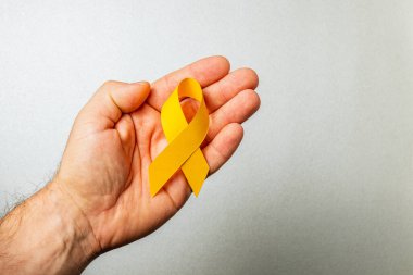 Bir kadın el, kanser önleme ve tedaviye verilen bilinci ve desteği simgeleyen sarı bir kurdele sergiliyor. Bu hareket, hastalıktan etkilenenler için dayanışma ve umudu yansıtıyor..