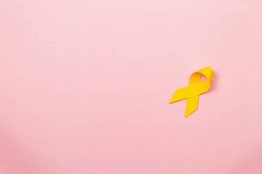 Sarı kurdele, kanserden etkilenenlerin farkındalığını ve desteğini sembolize eden yumuşak pembe bir zemine dayanır. Bu temsil cesaret, iyileşme ve toplum dayanışmasını teşvik eder..