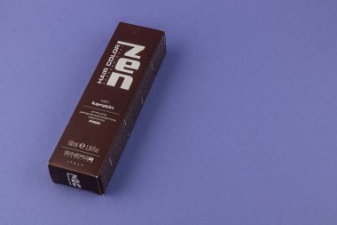 24.03.25 Lviv Ukrayna. Koyu kahverengi tonda keratin içeren bir kutu saç rengi ürünü. Paketleme basit bir mor arkaplan karşısında belirgin bir şekilde gösterilir.