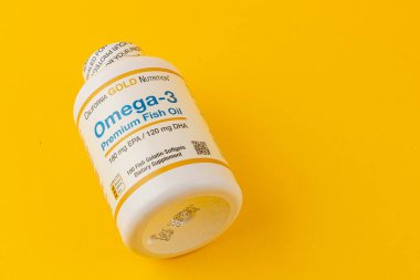 24.03.25 Lviv Ukrayna Bir şişe Omega-3 balık yağı softgels parlak sarı bir yüzey üzerinde durmaktadır. Etikette ürünün sağlık faydaları ve beslenme desteği için besin içeriği vurgulanıyor.