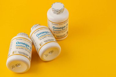 24.03.25 Lviv Ukrayna Üç şişe Omega-3 balık yağı kapsülü parlak sarı bir zemin üzerinde düzenlenmiştir, etiketleri ve sağlık faydaları çekici bir ortamda sergilenmektedir.