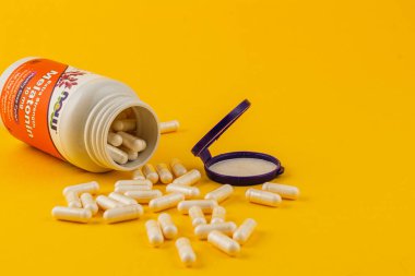 24.03.25 Lviv Ukrayna A vitamin kapsülü devrilerek parlak sarı bir zemin üzerine döküldü. Şişenin renkli bir etiketi var, canlı ekrana ekleniyor.
