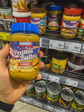 Lviv Ukrayna 24.03.25 Bir müşteri marketin koridorundan bir kavanoz kremalı fıstık ezmesi alır, gündüz alışverişi sırasında raflarda diğer gıda ürünleriyle çevrilidir..