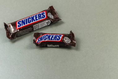 Lviv Ukrayna 04.02.25. Tarafsız gri bir yüzey üzerinde iki Snickers çikolatası sergilenir. Günün her saatinde atıştırmalık için mükemmel bir ikram sunar..