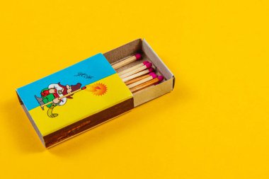 Lviv Ukrayna 04.02.25. Kapağında neşeli bir çizgi film karakteri olan canlı bir kibrit kutusu sarı bir arka planda oturuyor. Renkli kibritler kullanıma hazır..