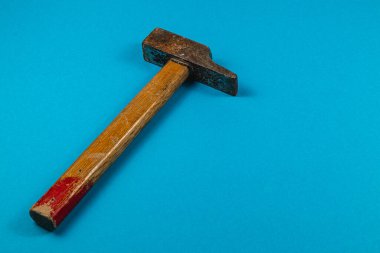 Ahşap saplı yıpranmış bir çekiç, parlak mavi bir yüzey üzerinde uzanır ve çeşitli atölye çalışmaları ve onarım işlerinde kullanıldığını gösterir..