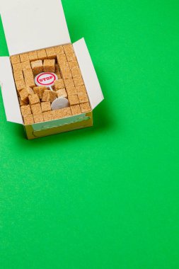 Kahverengi şeker küpleriyle dolu bir kutu açılır ve düzgünce düzenlenmiş tatlandırıcıyı ortaya çıkarır. Canlı yeşil arka plan sahneye yeni bir dokunuş katıyor..