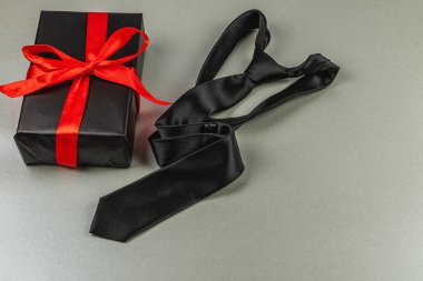 Siyah kravat, kırmızı kurdeleyle süslenmiş güzel paketlenmiş bir hediyenin yanında duruyor. Babalar Günü ya da doğum günü kutlaması için mükemmel. Babalar için bir minnettarlık sembolü..