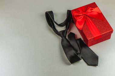 Süslü siyah bir kravat yanında güzel paketlenmiş kırmızı bir hediye kutusu duruyor. Yanında da mükemmel bir babalar günü kutlaması ya da doğum günü sürprizi var..