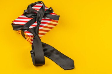 Büyük bir fiyonkla süslenmiş güzel paketlenmiş kırmızı bir hediye kutusu pembe bir arka planda oturur. Kutunun yanında iki şık siyah kravat duruyor. Babalar Günü için ideal.