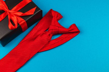 Canlı kırmızı bir kravat, babalar gününde neşe ve minnettarlığı simgeleyen kurdeleyle süslenmiş bir hediye kutusunun yanında duruyor. Bu ayar, babalar ve çocuklar arasındaki özel bağı vurgular..