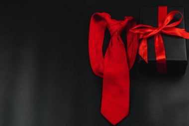 Kırmızı kurdeleli güzel paketlenmiş bir hediyenin yanında çarpıcı kırmızı bir kravat duruyor. Bu, babalar günü kutlamalarında babaları kalpten gelen hediyelerle onurlandırmak için mükemmel bir ipucu..