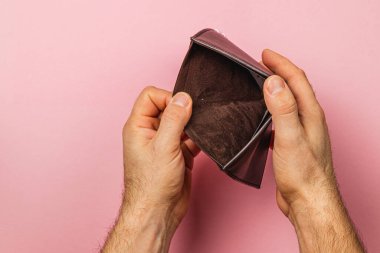 Erkek bir işadamı boş cüzdanını inceler, kaybını belli eder ve maddi durumu hakkında endişelenir. Pembe arka plan, bütçe sorunları ve ekonomik zorlukların katıksız gerçekliğini vurguluyor.