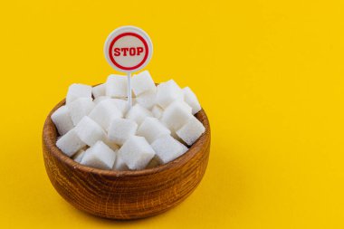 Tahta bir kase üzerinde küçük bir dur işareti olan bir sürü beyaz şeker küpü taşır. Kalın sarı arkaplan şekerli görüntünün çarpıcı görünümünü artırır.