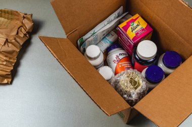 Lviv Ukrayna 10.04.25 Düz bir yüzeyde çeşitli sağlık malzemeleri ve vitaminlerle dolu bir karton kutu açılır. Ögeler arasında vitamin şişeleri ve beslenme ürünleri yer alıyor.